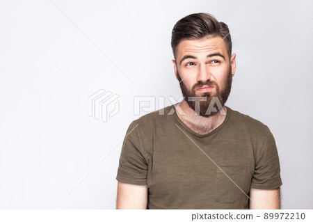 Portrait of thoughtful bearded man with dark green t shirt against light gray background. studio shot. . 89972210