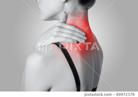Closeup view of a young woman with shoulder or neck pain on gray background. Black and white photo with red dot. Closeup view of a young woman with shoulder or neck pain on gray background. Black and white photo with red dot. 89972376