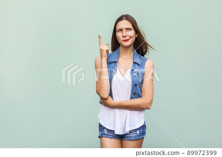 Pretty casual style girl with freckles got the idea and she raised her finger up and thinking. Isolated studio shot on light green background Pretty casual style girl with freckles got the idea and she raised her finger up and thinking. Isolated studio shot on light green background 89972399