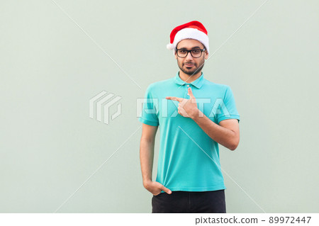 Businessman pointing copy space. Handsome man with beard in blue shirt looking at camera and pointing away while standing isolated on gray background. Studio shot 89972447