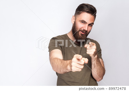 Hey you! Portrait of happy bearded man with dark green t shirt against light gray background. studio shot. . Hey you! Portrait of happy bearded man with dark green t shirt against light gray background. studio shot. . 89972478
