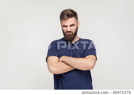 Resentful man, with arms folded, over gray background in studio shot and offended looked at camera. 89972479