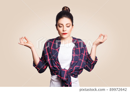 Meditation, religion and spiritual practises. Beautiful young brunette girl doing yoga in the morning indoors at beige wall after waking up, keeping eyes closed, holding fingers in mudra gesture Meditation, religion and spiritual practises. Beautiful young brunette girl doing yoga in the morning indoors at beige wall after waking up, keeping eyes closed, holding fingers in mudra gesture 89972642