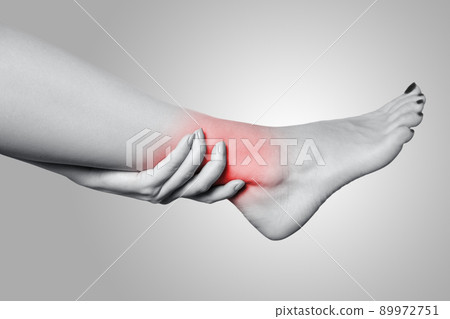 Closeup view of a young woman with pain on leg on gray background. Black and white photo with red dot. Closeup view of a young woman with pain on leg on gray background. Black and white photo with red dot. 89972751
