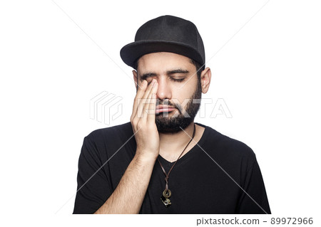Portrait of young unhappy sad man with black t-shirt and cap looking at camera crying closed eyes. studio shot, isolated on white background. Portrait of young unhappy sad man with black t-shirt and cap looking at camera crying closed eyes. studio shot, isolated on white background. 89972966