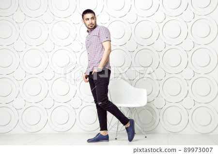 Young bearded fashion model in casual style is posing near white circle wall background. studio shot. posing and looking away with hand on packet. Young bearded fashion model in casual style is posing near white circle wall background. studio shot. posing and looking away with hand on packet. 89973007
