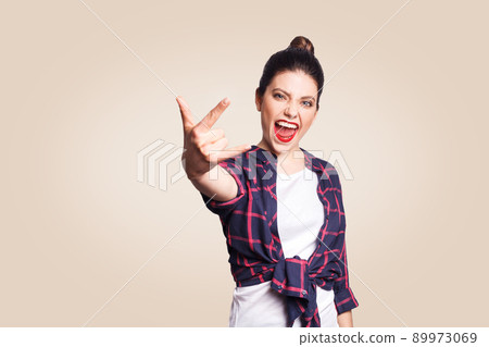 Rock sign. Happy funny toothy smiley young woman showing Rock sign with fingers. studio shot on beige background. focus on face. 89973069
