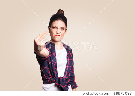 Middle finger sign. Unhappy angry young woman showing middle finger with unsatisfied face. studio shot on beige background. focus on face. 89973088