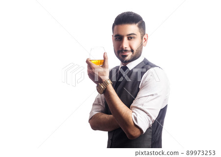 Handsome bearded businessman holding a glass of whiskey. holding glass, smiling and looking at camera. studio shot, isolated on white background. 89973253