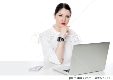 Portrait of serious successful brunette businesswoman in white shirt sitting with laptop, touhing her chin and looking at camera with thoughtful face. indoor studio shot, isolated in white background. 89973255