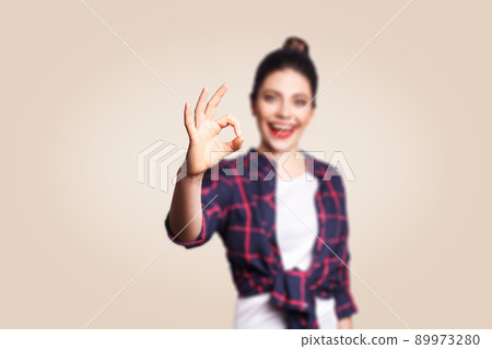 OK. Happy toothy smiley young woman showing OK sign with fingers. studio shot on beige background. focus on hand. OK. Happy toothy smiley young woman showing OK sign with fingers. studio shot on beige background. focus on hand. 89973280