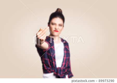 Middle finger sign. Unhappy angry young woman showing middle finger with unsatisfied face. studio shot on beige background. focus on fingers. 89973290