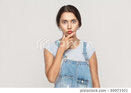 Amazed hispanic woman looking at camera with big eyes and touching her chin. Studio shot, isolated on gray background Amazed hispanic woman looking at camera with big eyes and touching her chin. Studio shot, isolated on gray background 89973301