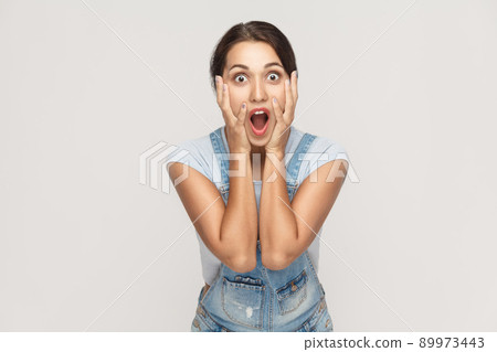 Human face expressions and emotions. Arab young adult woman holding arms on her cheeks and shocked. Isolated on gray background, studio shot Human face expressions and emotions. Arab young adult woman holding arms on her cheeks and shocked. Isolated on gray background, studio shot 89973443