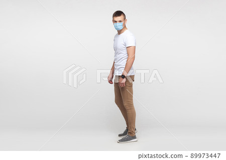 Protection against contagious disease, coronavirus. full length portrait of young man wearing hygienic mask to prevent infection, Covid-2019. indoor studio shot isolated on gray background Protection against contagious disease, coronavirus. full length portrait of young man wearing hygienic mask to prevent infection, Covid-2019. indoor studio shot isolated on gray background 89973447