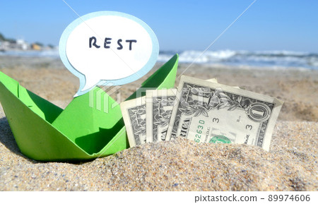 Small blue paper boat, three one paper dollar bills and speech bubble with word Rest on sandy sea beach on sunny summer day. Concept money finance business tourism travel dreams vacation holiday 89974606