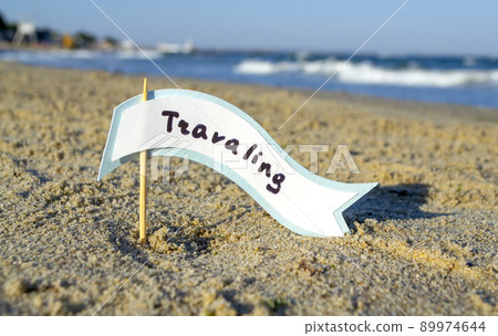 Small stick with paper speech bubble with word Traveling stands on sandy beach near sea water and sea waves with white foam close-up. Concept of travel, tourism, vacation, holiday, relax, rest, summer Small stick with paper speech bubble with word Traveling stands on sandy beach near sea water and sea waves with white foam close-up. Concept of travel, tourism, vacation, holiday, relax, rest, summer 89974644