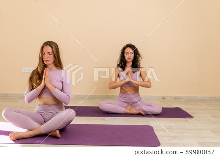 Well looking middle aged sporty woman, fitness instructor in pink sportswear doing stretching and pilates on yoga mat in the studio with mirror. Female fitness yoga. Healthy lifestyle and harmony. Well looking middle aged sporty woman, fitness instructor in pink sportswear doing stretching and pilates on yoga mat in the studio with mirror. Female fitness yoga. Healthy lifestyle and harmony. 89980032