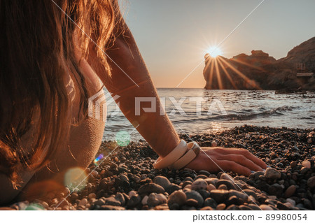 Young woman with long hair in white swimsuit and boho style braclets practicing outdoors on yoga mat by the sea on a sunset. Women's yoga fitness routine. Healthy lifestyle, harmony and meditation Young woman with long hair in white swimsuit and boho style braclets practicing outdoors on yoga mat by the sea on a sunset. Women's yoga fitness routine. Healthy lifestyle, harmony and meditation 89980054