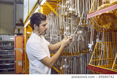 Young man shopping at a DIY store and trying to choose a new stainless steel hose Young man shopping at a DIY store and trying to choose a new stainless steel hose 89980742