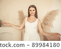 young girl stands and looks at camera, and behind her back is an ornamental plant in form of angel wings 89984180