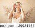 young girl stands and looks at camera, and behind her back is an ornamental plant in form of angel wings 89984184