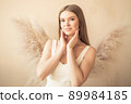 young girl stands and looks at camera, and behind her back is an ornamental plant in form of angel wings 89984185