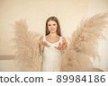 young girl stands and looks at camera, and behind her back is an ornamental plant in form of angel wings 89984186