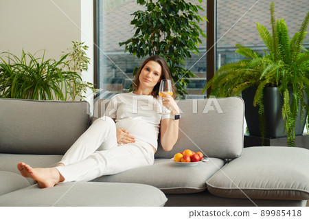 Cute woman on sofa with a glass of fresh orange juice Cute woman on sofa with a glass of fresh orange juice 89985418
