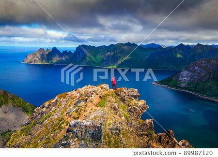 Hiker standing on the top of Husfjellet Mountain on Senja Island in Norway 89987120
