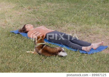 a European woman with meditates in the park with her dog on a blue yoga mat. shavasana and meditation for mental and physical health 89987125