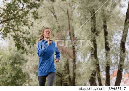 a European woman in a blue hoodie is running and doing sports in the park. fitness and yoga outdoor sports 89987147