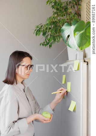 a woman makes notes on colored stickers on the refrigerator. a reminder or a note for her husband and children a woman makes notes on colored stickers on the refrigerator. a reminder or a note for her husband and children 89987161