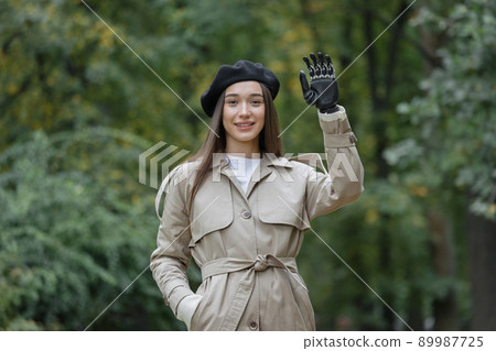 a happy European cyber woman with a bionic prosthesis on her arm waves to her friends. disability or amputation of limbs 89987725