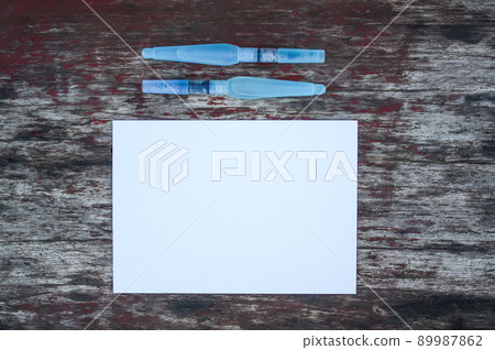 White paper sheet and water brushes on wooden background. 89987862
