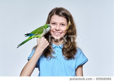 Child girl with pet green quaker parrot looking at camera on light studio background Child girl with pet green quaker parrot looking at camera on light studio background 89988066