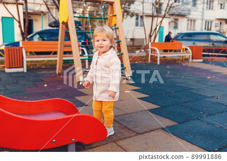 A little cute girl is standing near the children's slide on the playground. The concept of childhood and autism 89991886