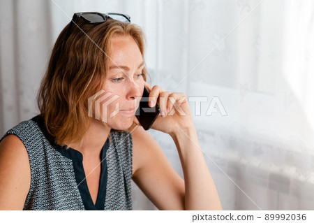 Remote work. The woman works at home at the computer, and talks on the phone. The concept of quarantine, freelancing, and self-isolation 89992036