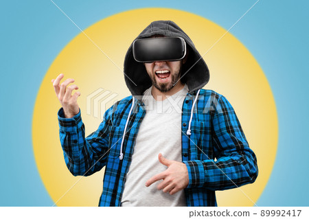 A man happily plays an imaginary guitar with the help of VR glasses. Yellow-blue background in the background. Virtual Reality Concept A man happily plays an imaginary guitar with the help of VR glasses. Yellow-blue background in the background. Virtual Reality Concept 89992417