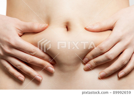 A woman holds her hands to her stomach, pulling the skin with fat. Close-up of the abdomen and navel. The concept of obesity, weight loss and liposuction A woman holds her hands to her stomach, pulling the skin with fat. Close-up of the abdomen and navel. The concept of obesity, weight loss and liposuction 89992659
