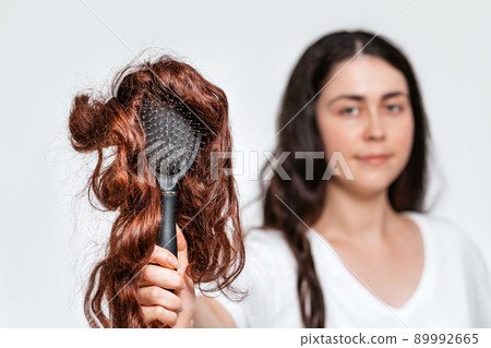 Blurred portrait of a woman holds a comb with a wig on it. White background. Concept of hair care and hair loss Blurred portrait of a woman holds a comb with a wig on it. White background. Concept of hair care and hair loss 89992665