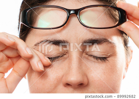 Ophthalmology. Close-up of woman's face scratches her painful eyes, taking off her glasses. The concept of unhealthy eyes and vision Ophthalmology. Close-up of woman's face scratches her painful eyes, taking off her glasses. The concept of unhealthy eyes and vision 89992682
