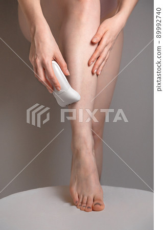 A young woman removes excess hair with a depilator. Concept of home skin care and Spa. Smooth slender legs 89992740