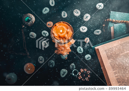 Astrology and esotericism. On a black background lie fortune-telling runes, a book, precious amulets, a copper lamp and a candle. Dust and light Astrology and esotericism. On a black background lie fortune-telling runes, a book, precious amulets, a copper lamp and a candle. Dust and light 89993464