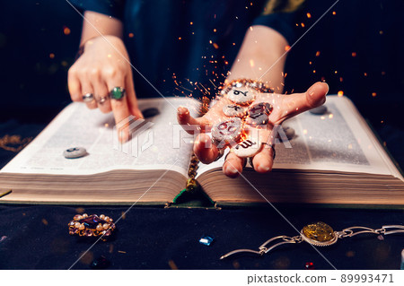 Fortune teller's hand holds the sparkling zodiac stones in the palm of her hand over the open book. The concept of divination and magic 89993471
