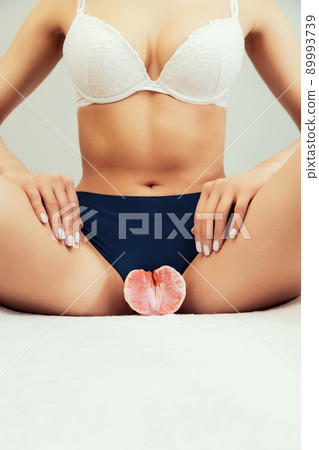 A woman holds half a grapefruit near the intimate area. Close-up. Vertical. Copy space. The concept of gynecological problems A woman holds half a grapefruit near the intimate area. Close-up. Vertical. Copy space. The concept of gynecological problems 89993739