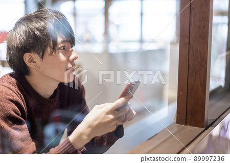 一個二十多歲的男人在咖啡館的窗邊操作智能手機 一個二十多歲的男人在咖啡館的窗邊操作智能手機 89997236