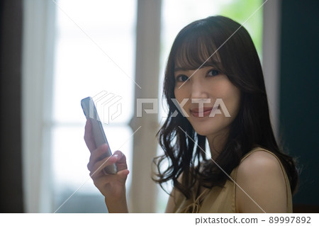 Lifestyle image of a young woman operating a smartphone in a room 89997892