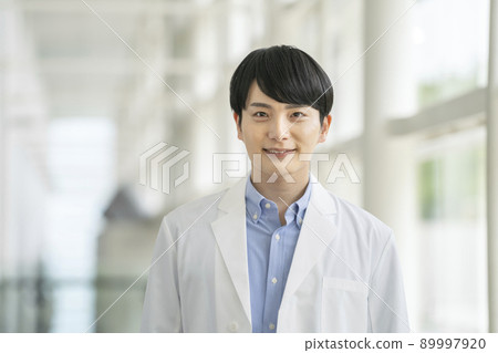 一名 20 多歲的男性理科學生/醫務工作者/研究員穿著白大褂微笑著看著相機的照片 一名 20 多歲的男性理科學生/醫務工作者/研究員穿著白大褂微笑著看著相機的照片 89997920