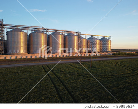 Grain elevator. Metal grain elevator in agricultural zone. Agriculture storage for harvest. Grain silos on green nature background. Exterior of agricultural factory. Nobody. 89999634